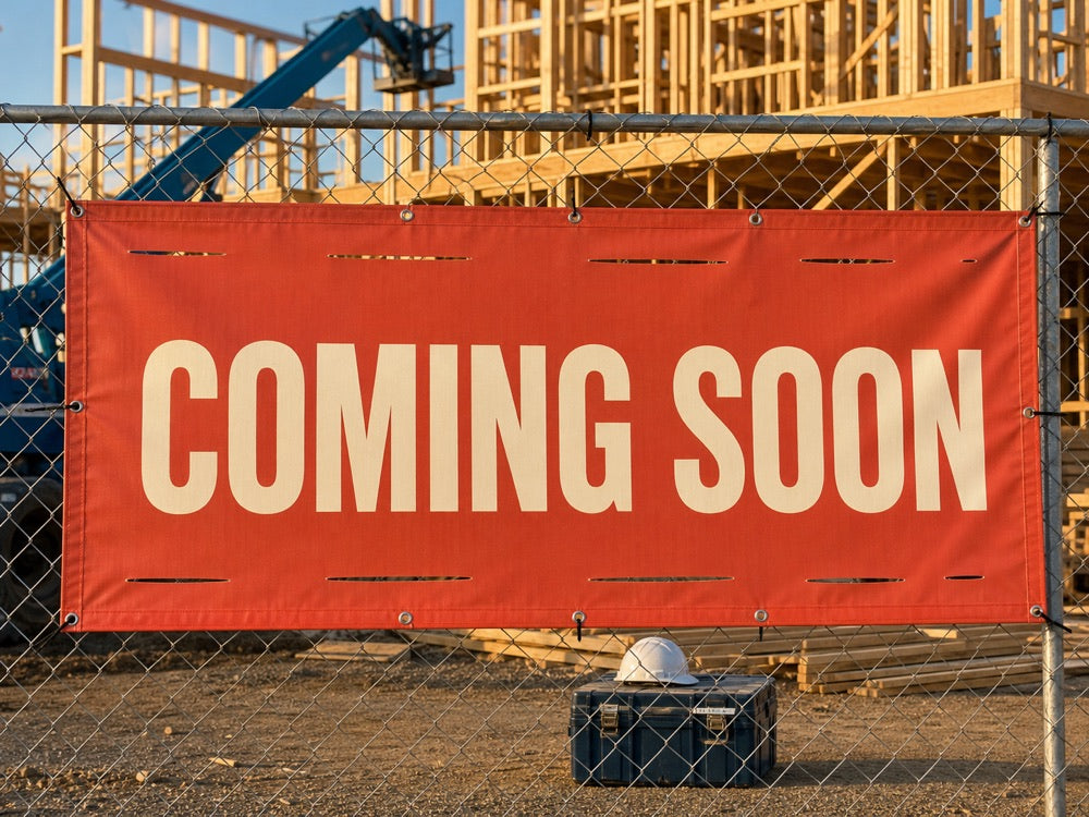 COMING SOON banner with wind slits zip-tied to a construction site fence